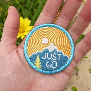 Może przedstawiać: Naszywka haftowana w kolorze niebieskim i żółtym z motywem górskim i napisem "JUST GO".