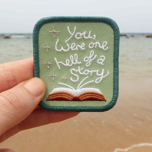 May include: A green embroidered patch with a white open book and the text "You were one hell of a story".