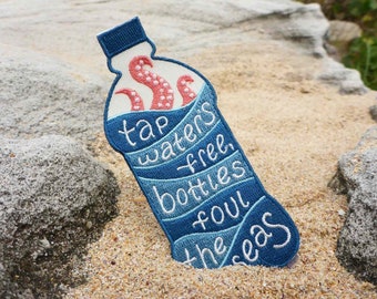 Può includere: Toppa ricamata blu e bianca a forma di bottiglia d'acqua con un polpo rosso all'interno. La toppa dice "Tap waters free, bottles foul the seas".