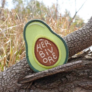 May include: A green avocado-shaped patch with brown embroidery that reads "HER BIV ORE".