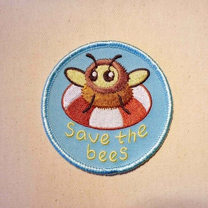 May include: A blue and white embroidered patch with a cartoon bee wearing a life preserver. The text "Save the bees" is written below the bee.
