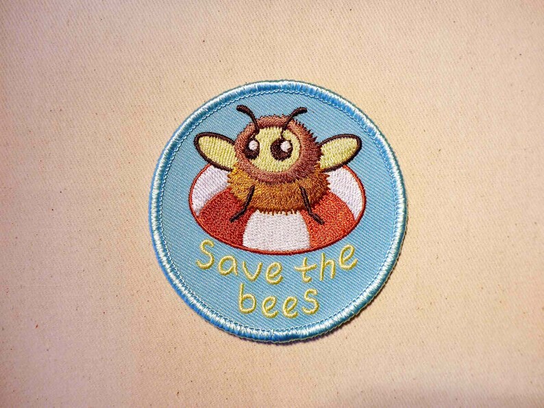 May include: A blue and white embroidered patch with a cartoon bee wearing a life preserver. The text "Save the bees" is written below the bee.