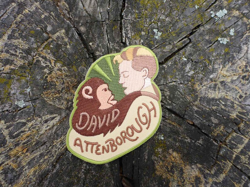 K&ouml;nnte beinhalten: Gestickter Aufn&auml;her mit einer Cartoon-Illustration von David Attenborough mit einem Affen, mit dem Text "David Attenborough" in braunem Garn.