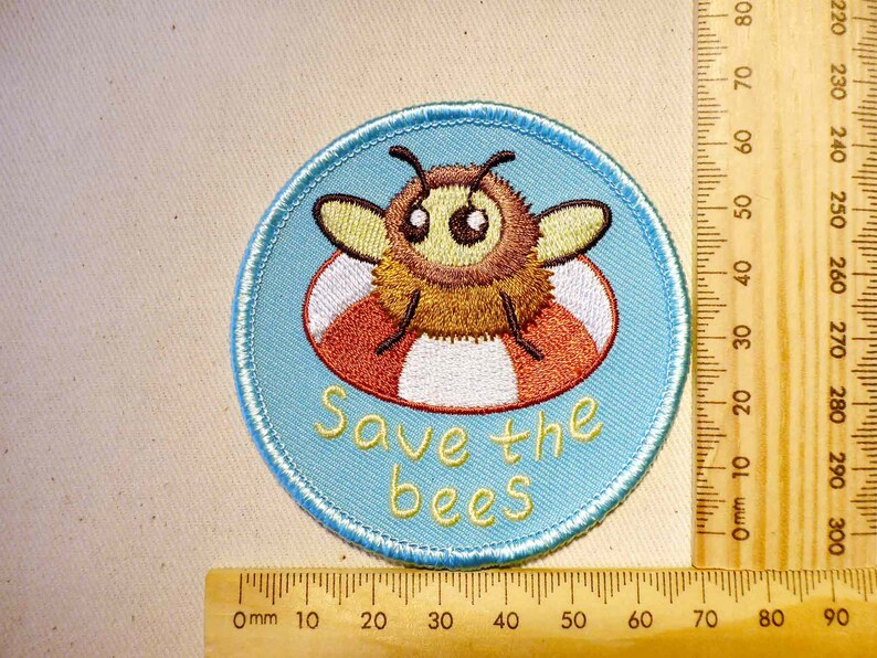 May include: A blue and white embroidered patch with a cartoon bee wearing a red and white life preserver. The text "Save the bees" is written below the bee.