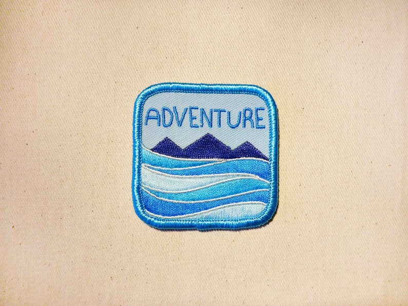 May include: Blue and white embroidered patch with the word "ADVENTURE" in white text and a blue mountain range and waves design.