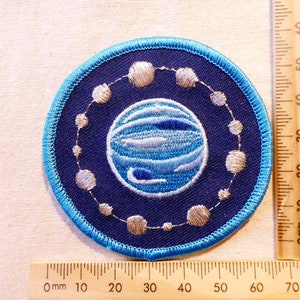 May include: A blue and white embroidered patch featuring a planet with a ring of stars around it.