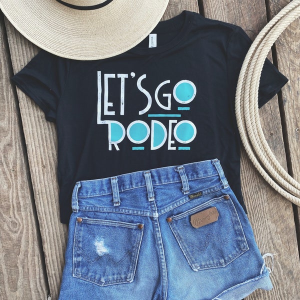 May include: Black t-shirt with the text "Let's Go Rodeo" in white and blue lettering. The shirt is paired with denim shorts and a straw hat.