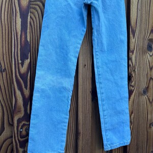 May include: Light blue denim jeans with a classic five-pocket design. The jeans have a straight leg cut and a faded wash, with visible stitching details. The Wrangler brand label is visible on the back pocket.