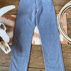May include: A pair of light gray denim jeans with a straight leg fit. The jeans have a button fly and five pockets.