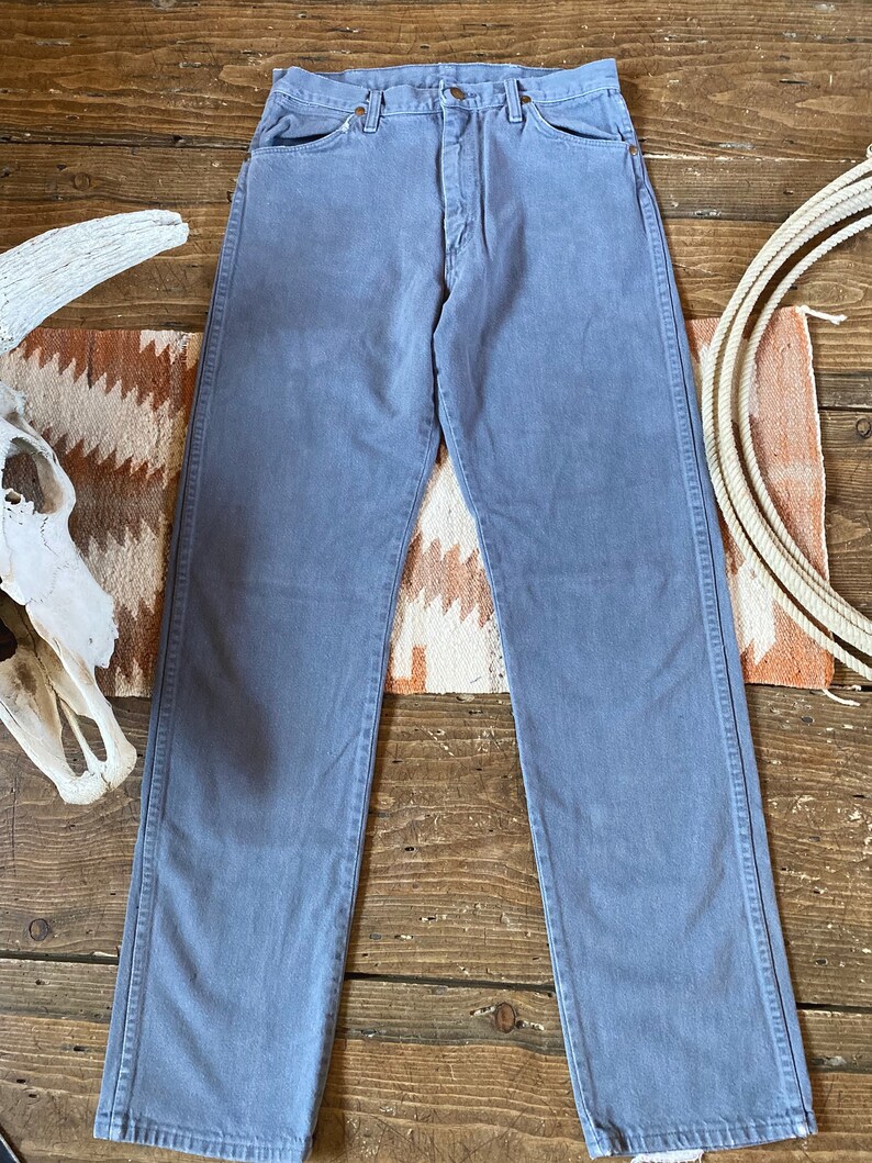 May include: A pair of light gray denim jeans with a straight leg fit. The jeans have a button fly and five pockets.
