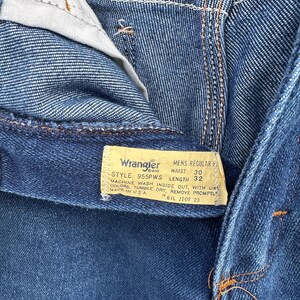 Puede incluir: Un vaquero azul de mezclilla Wrangler para hombre, de corte regular, con una etiqueta de cuero marr&oacute;n. La etiqueta tiene el texto "Wrangler Brand", "Mens Regular Fit", "Style 955PWS", "Waist 30", "Length 32", "Machine Wash Inside Out, With Like Colors, Tumble Dry, Remove Promptly", "Made in USA", "R6IL J109 23".