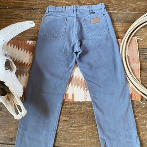 May include: A pair of light blue denim jeans with a brown leather patch on the back pocket that says "Wrangler".