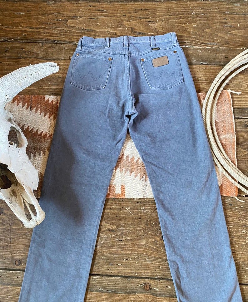 May include: A pair of light blue denim jeans with a brown leather patch on the back pocket that says "Wrangler".