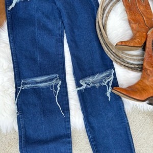 May include: A pair of dark blue denim jeans with distressed details, featuring several rips and frayed edges on the knees and thighs.