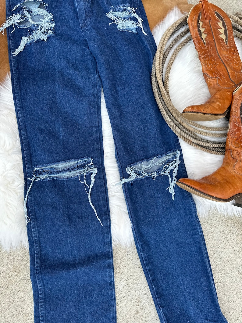 May include: A pair of dark blue denim jeans with distressed details, featuring several rips and frayed edges on the knees and thighs.
