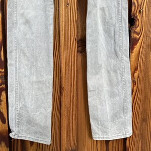 Pu&ograve; includere: Jeans in denim grigio chiaro con taglio dritto. I jeans hanno un classico design a cinque tasche e una chiusura con bottone e cerniera. Il tessuto sembra essere prelavato, conferendogli un aspetto morbido. I jeans sono esposti su uno sfondo di legno.