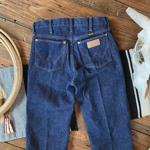 May include: A pair of dark blue denim jeans with a classic straight leg fit. The jeans have a leather patch on the back with the Wrangler logo.