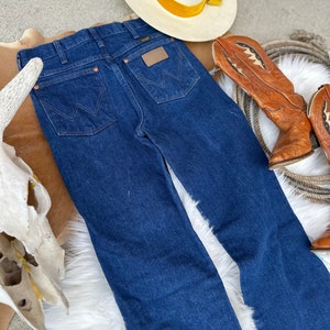 May include: A pair of dark blue denim jeans with a brown leather patch on the back pocket that says "Wrangler".