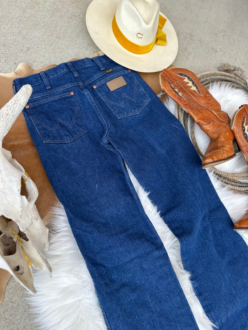 May include: A pair of dark blue denim jeans with a brown leather patch on the back pocket that says "Wrangler".