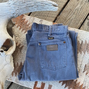 May include: A pair of folded blue denim jeans with a brown leather Wrangler label on the back pocket.