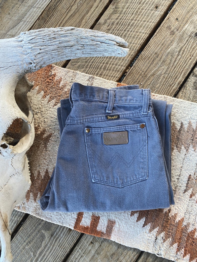 May include: A pair of folded blue denim jeans with a brown leather Wrangler label on the back pocket.