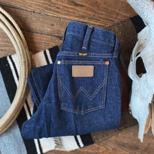 May include: A pair of dark blue denim jeans with a brown leather patch that says "Wrangler" on the back pocket.