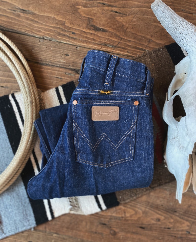 May include: A pair of dark blue denim jeans with a brown leather patch that says "Wrangler" on the back pocket.