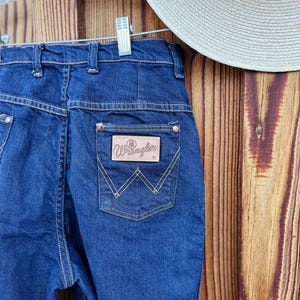 May include: A pair of dark blue denim jeans with a brown leather patch on the back pocket that says "Wrangler".