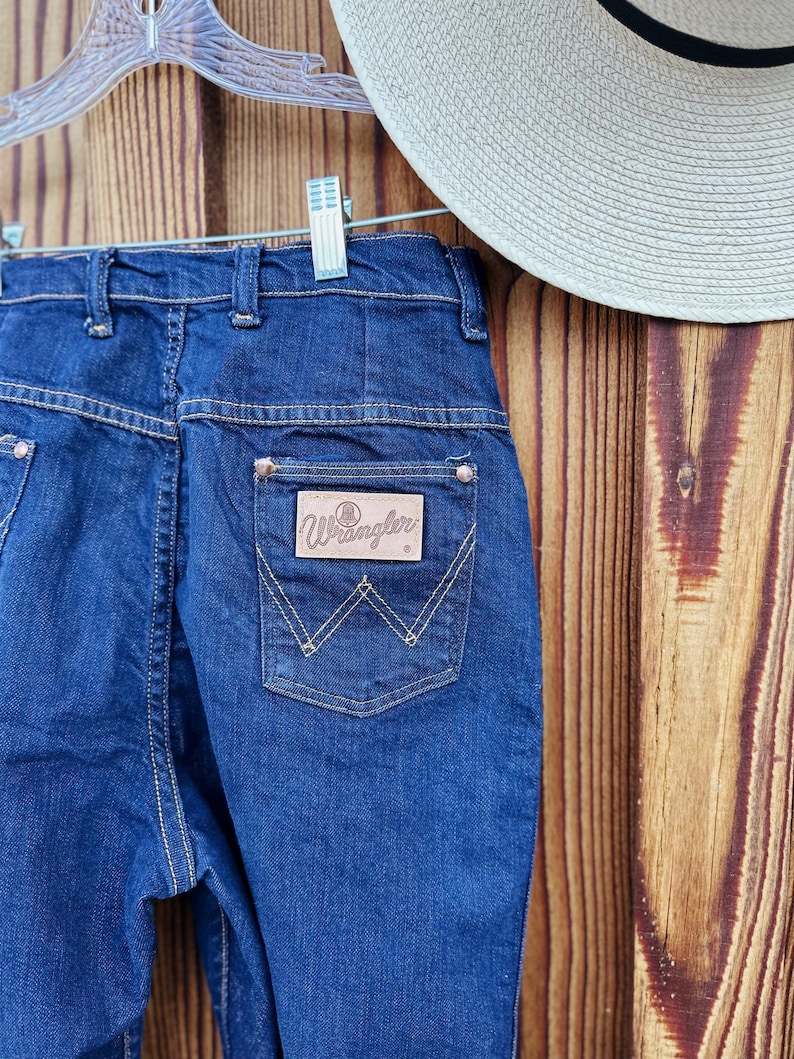 May include: A pair of dark blue denim jeans with a brown leather patch on the back pocket that says "Wrangler".