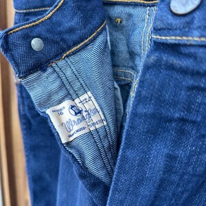 May include: Close-up of the inside of a pair of blue denim jeans. The jeans have a Wrangler label that says "Sanforized Stretch" and "Made in U.S.A.". The label also says "Misses 16".