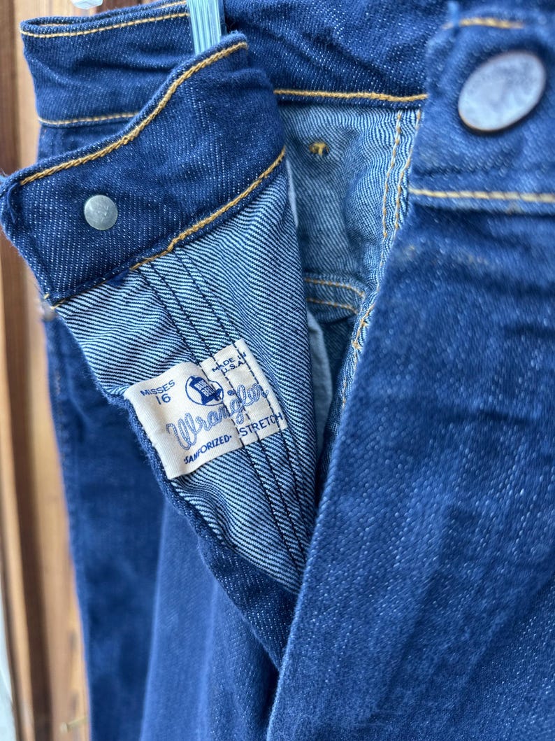 May include: Close-up of the inside of a pair of blue denim jeans. The jeans have a Wrangler label that says "Sanforized Stretch" and "Made in U.S.A.". The label also says "Misses 16".