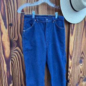 May include: A pair of dark blue denim jeans with a high waist and a straight leg. The jeans have a classic five-pocket style and a button fly.