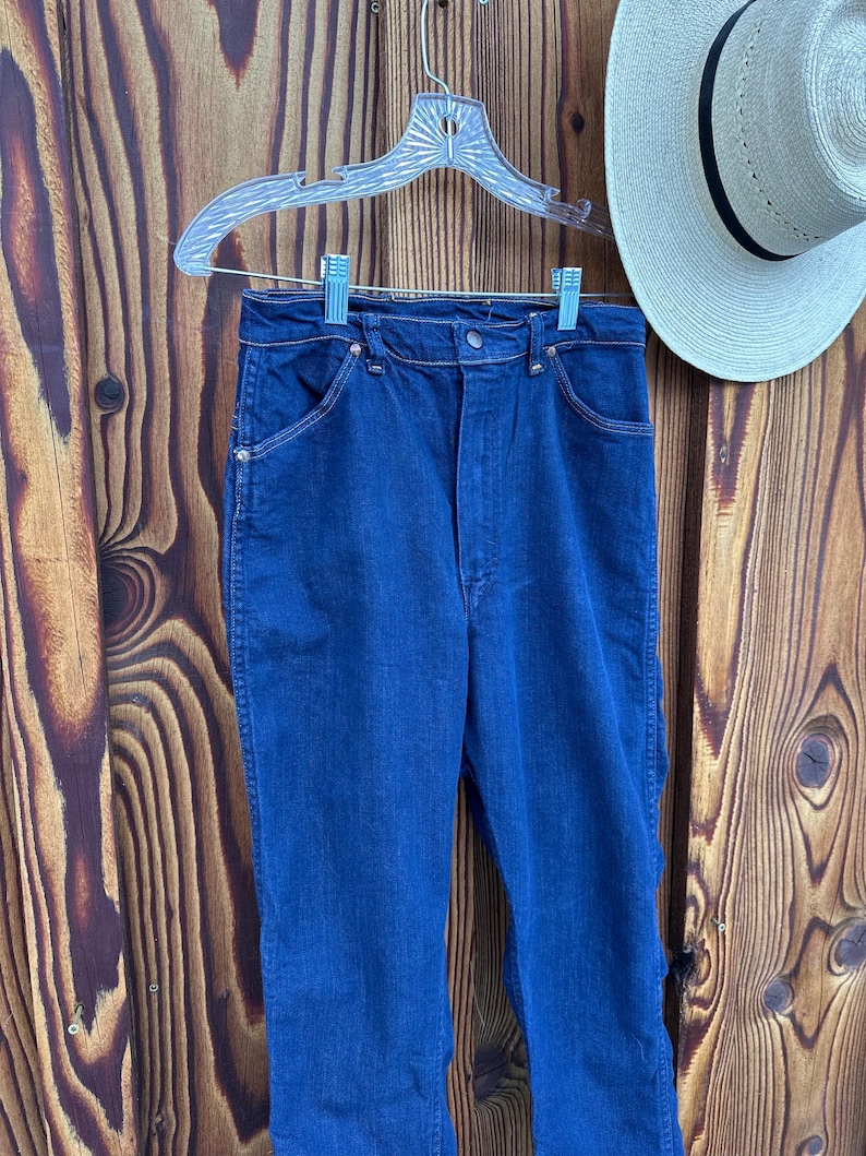 May include: A pair of dark blue denim jeans with a high waist and a straight leg. The jeans have a classic five-pocket style and a button fly.