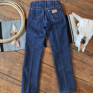 May include: A pair of dark blue denim jeans with a brown leather patch on the back pocket that says "Wrangler".