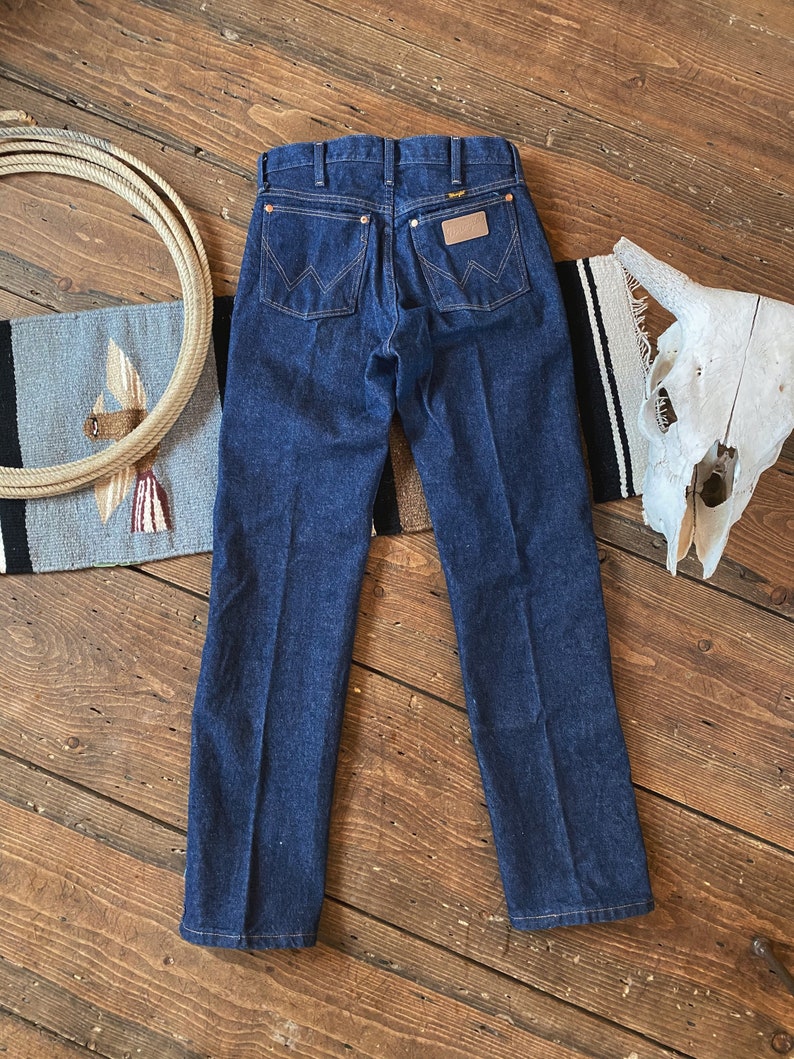 May include: A pair of dark blue denim jeans with a brown leather patch on the back pocket that says "Wrangler".