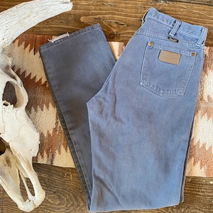 May include: A pair of gray denim jeans with a brown leather patch on the back pocket that says "Wrangler".