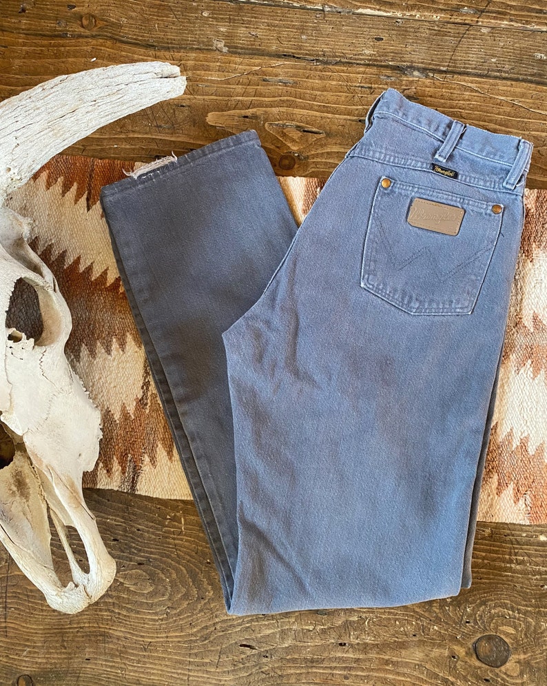 May include: A pair of gray denim jeans with a brown leather patch on the back pocket that says "Wrangler".