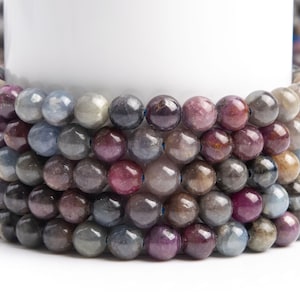 Op de afbeelding: Een streng multi-kleurige edelsteen kralen, met tinten blauw, paars en roze. De kralen zijn rond en glad, en ze zijn aan elkaar geregen op een heldere draad.