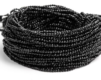 May include: A strand of black faceted gemstone beads. The beads are small and round, and they are strung together on a thin thread. The beads are arranged in a coil, and they are all the same size and shape.