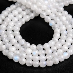 May include: A strand of white moonstone beads, with a subtle iridescent sheen. The beads are round and smooth, and they are strung on a clear thread.