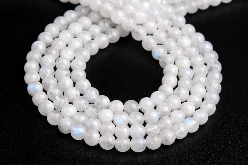 May include: A strand of white moonstone beads, with a subtle iridescent sheen. The beads are round and smooth, and they are strung on a clear thread.