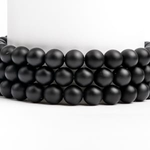 May include: A close-up of three strands of black matte beads. The beads are round and smooth, and they are arranged in a circular pattern.