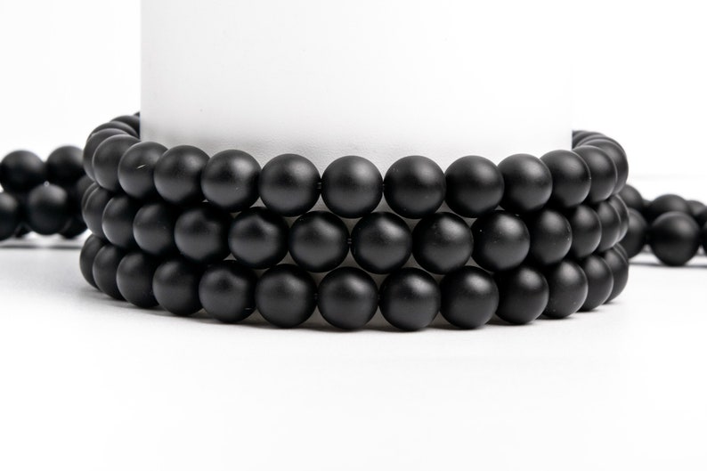 May include: A close-up of three strands of black matte beads. The beads are round and smooth, and they are arranged in a circular pattern.