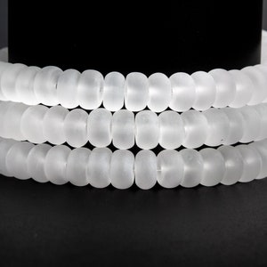 May include: A white frosted glass bead necklace with multiple strands of beads. The necklace is coiled on a black surface.