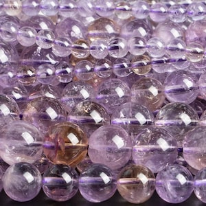 May include: A strand of round, translucent amethyst beads in shades of light and dark purple. The beads have a smooth, polished finish and are strung on a clear thread.