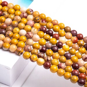 May include: A strand of round, yellow, brown, and red gemstone beads. The beads are smooth and polished, and they have a natural, earthy look.
