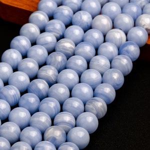 May include: A strand of light blue agate beads with white and gray swirls. The beads are round and smooth, and they are strung on a clear thread.