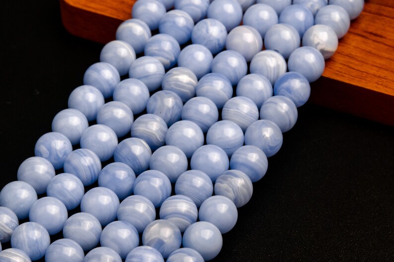 May include: A strand of light blue agate beads with white and gray swirls. The beads are round and smooth, and they are strung on a clear thread.