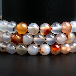 May include: A strand of white agate beads with brown and orange agate beads interspersed. The beads are round and smooth.