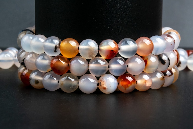 May include: A strand of white agate beads with brown and orange agate beads interspersed. The beads are round and smooth.